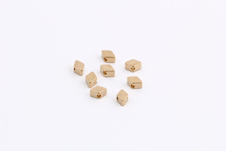 May include: A group of ten gold-colored metal diamond-shaped beads with a small hole in the center of each bead.