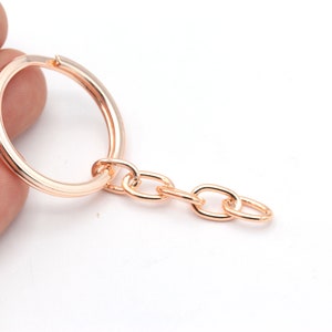 May include: A rose gold key ring with a round metal ring and a chain attached.