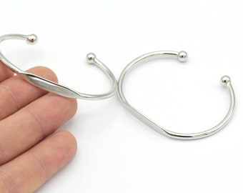 May include: Two silver bangle bracelets with rounded ends. The bracelets are open and have a flat, slightly curved section in the middle.