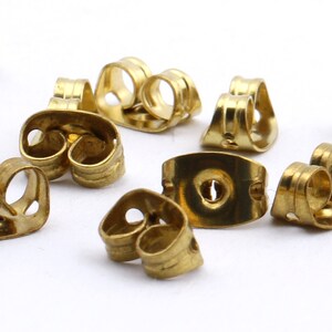 May include: A close-up of a group of gold-colored earring backs. The backs are made of metal and have a variety of shapes and sizes.