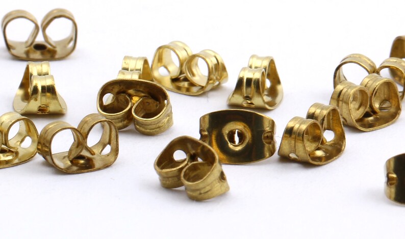 May include: A close-up of a group of gold-colored earring backs. The backs are made of metal and have a variety of shapes and sizes.