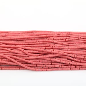 Puede incluir: Una hebra de cuentas de vidrio rosa, cada cuenta es un pequeño cilindro con una sección transversal cuadrada.