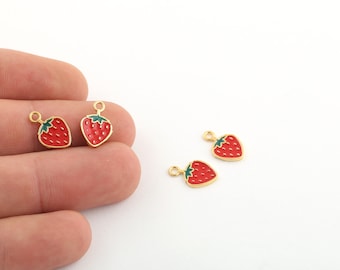 May include: Four gold-colored metal charms shaped like strawberries. The strawberries are red with green leaves and have a small loop at the top for attaching to jewelry or other crafts.