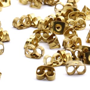May include: A pile of gold-colored earring backs. The backs are made of metal and have a small hole in the center. They are designed to be used with stud earrings.