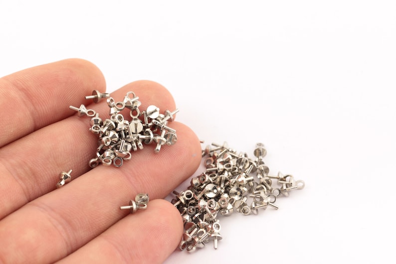 K&ouml;nnte beinhalten: Ein Haufen silberfarbener Metallperlenspitzen mit einer &Ouml;se an einem Ende und einer kleinen Schraube am anderen Ende.