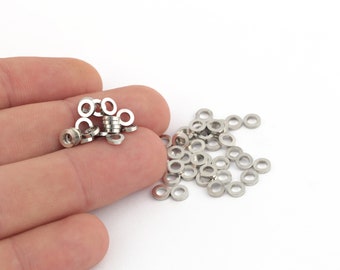 May include: A close-up of a pile of silver metal washers. The washers are small and round, with a hole in the center. There are about 50 washers in the pile.
