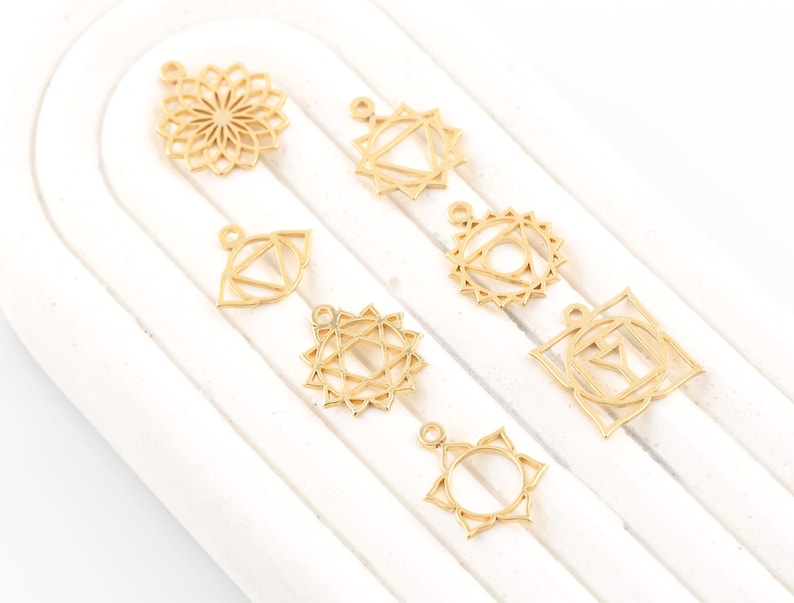 May include: Seven gold-colored metal charms featuring different chakra symbols. The charms are designed with intricate details and are perfect for jewelry making.