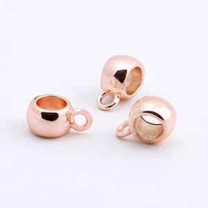 May include: Three rose gold metal bead caps with a small loop on the top. The bead caps are designed to be used as a decorative element for jewelry making.