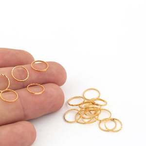 Puede incluir: Un montón de anillos de salto de color dorado, algunos están en un dedo, otros están en una pila sobre una superficie blanca.