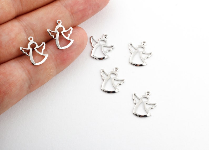 May include: Six silver angel charms with a cutout design. The charms are scattered on a white surface.