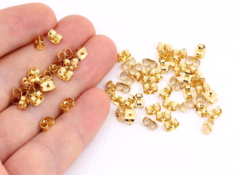 May include: A large quantity of gold-colored earring backs. The backs are made of metal and have a double-prong design.