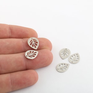 Könnte beinhalten: Fünf silberne Metall-Blätter-Anhänger mit einem ausgeschnittenen Design. Die Anhänger haben oben ein Loch zum Anbringen an Schmuck oder anderen Bastelarbeiten.
