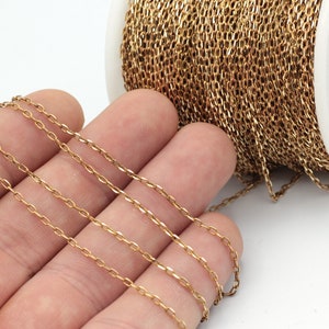 May include: A spool of gold-coloured chain, with a portion of the chain draped over a hand. The chain is made of small, oval-shaped links.