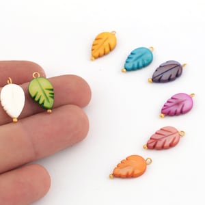 May include: Assortment of colorful leaf-shaped charms with gold accents. The charms are made of a smooth, iridescent material and have a delicate, carved leaf design.