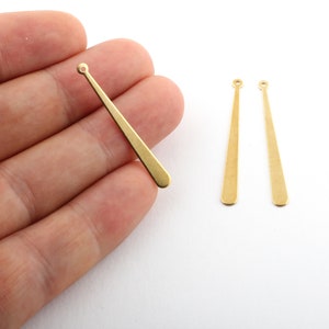 May include: Three gold-colored metal earring findings with a loop at the top and a pointed end. The findings are about 1.5 inches long.