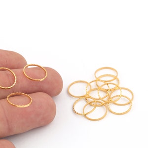 May include: A pile of gold-colored metal rings with a textured surface. The rings are arranged in a loose pile on a white background.