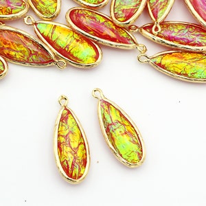 May include: A group of 18 gold-rimmed teardrop-shaped glass beads with a red and green iridescent finish. The beads have a gold loop at the top for attaching to jewelry.
