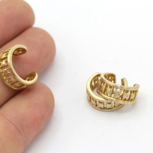 May include: Two gold ear cuffs with a decorative design. The cuffs are made of metal and have a smooth finish.