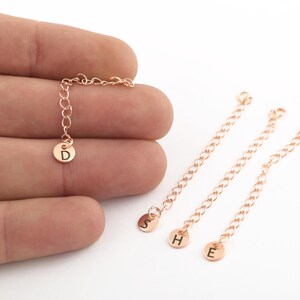 May include: Three gold-toned chains with small round charms attached to the ends. The charms are engraved with the letters D, H, and E.
