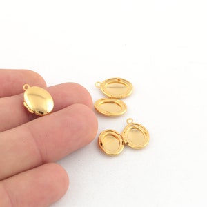 Op de afbeelding: Vier gouden ovale medaillon hangers met scharnieren. De medaillons zijn open en gesloten, waardoor de binnenkant van de medaillons zichtbaar is.