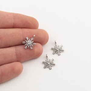 Op de afbeelding: Drie zilveren sneeuwvlokcharms met heldere kristallen accenten. De charms zijn op een witte achtergrond.