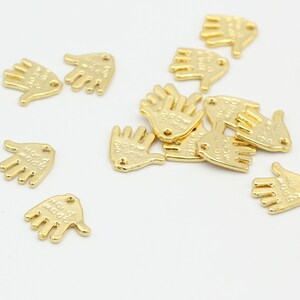May include: A group of gold-colored metal hand charms with the words "Hold My Hand" engraved on them.