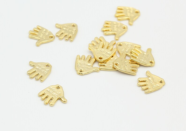 May include: A group of gold-colored metal hand charms with the words "Hold My Hand" engraved on them.