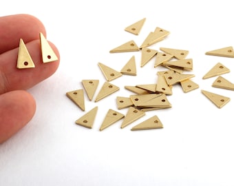 May include: A group of small, gold-coloured triangle-shaped metal charms with a hole at the top. The charms are scattered on a white surface.