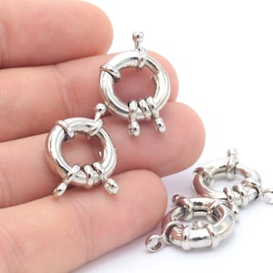 May include: Three silver-toned metal clasps, each with a round ring and decorative details. The clasps are designed for attaching jewelry or other items.