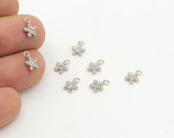May include: Eight silver snowflake charms with clear crystal accents. The charms have a loop at the top for attaching to jewellery or other crafts.