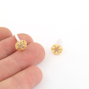 May include: A pair of gold-toned earrings with clear rhinestone accents in the shape of a flower.
