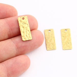 Puede incluir: Tres etiquetas rectangulares de metal de color dorado con textura martillada y un agujero en la parte superior para colgar.