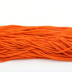 May include: A close-up of a pile of orange seed beads. The beads are small and round, and they are arranged in a random pattern.
