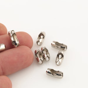 Op de afbeelding: Zilveren metalen kettingverbinders, ook wel kettingschakels genoemd, worden getoond op een wit oppervlak. De verbinders zijn klein en cilindrisch van vorm, met een gedraaid ontwerp.