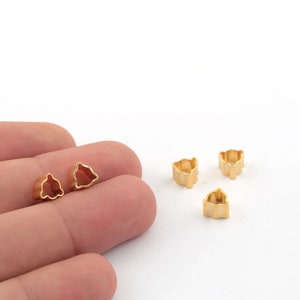 May include: Five gold-colored metal charms in the shape of a bell. The charms are small and have a smooth, shiny finish.