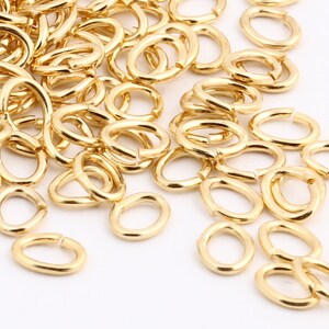 May include: A large pile of gold-coloured metal jump rings. The rings are oval shaped and are scattered on a white surface.