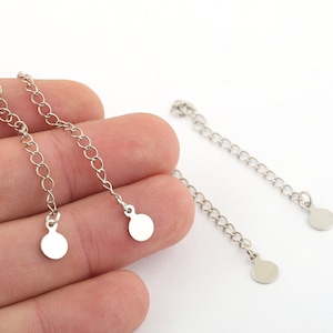 May include: Two silver chain extenders with round disc ends. The extenders are approximately 2 inches long.