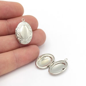 Op de afbeelding: Twee zilveren ovale medaillon hangers met een scharnieropening. Een medaillon is gesloten en de andere is open, waardoor de binnenkant van het medaillon zichtbaar is.