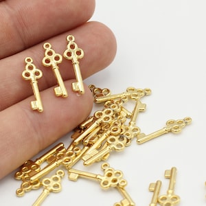 May include: A pile of gold-toned metal key charms with intricate designs. The keys have a circular pattern at the top and a straight shaft.