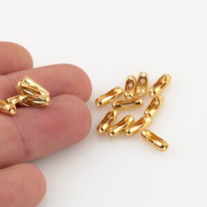 Op de afbeelding: Een close-up van een stapel gouden metalen kettingschakels. De schakels zijn klein en cilindrisch, met een lichte draai in het midden. Ze zijn perfect om een ​​toets van elegantie toe te voegen aan sieraden of andere ambachten.