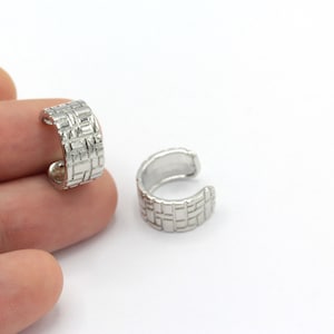 May include: Two silver ear cuffs with a geometric pattern. The cuffs are open and can be adjusted to fit different ear sizes.