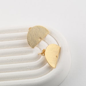 May include: A pair of gold-toned half-circle earrings with a textured finish. The earrings have a small hole in the center for attaching to an earring post.