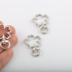 May include: Three silver metal keychains shaped like four-leaf clovers. Each keychain has a swiveling ring at the bottom.