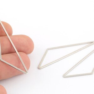 Pode incluir: Três pingentes geométricos prateados com forma triangular e um laço na parte superior para prender em joias.