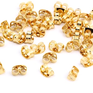 May include: A large group of gold-colored earring backs. The backs are made of metal and have a small loop on each side.