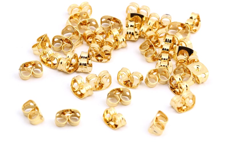 May include: A large group of gold-colored earring backs. The backs are made of metal and have a small loop on each side.