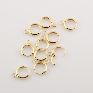 May include: A group of ten gold-colored earring hoops, all of the same size and style, are scattered on a white surface.