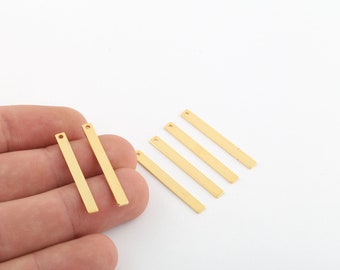 May include: Six gold-colored metal bar pendants with a small hole at the top. The pendants are arranged in a staggered pattern on a white surface.