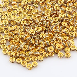 May include: A large pile of gold-toned metal bead caps with clear rhinestones around the edges. The bead caps are scattered on a white surface.