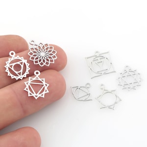 Könnte beinhalten: Ein Set mit sieben silbernen Metall-Anhängern mit verschiedenen Chakra-Symbolen. Die Anhänger sind in Form eines Kreises, Quadrats und Sterns. Die Anhänger sind perfekt für die Schmuckherstellung oder um Ihren Bastelarbeiten einen Hauch von Spiritualität zu verleihen.